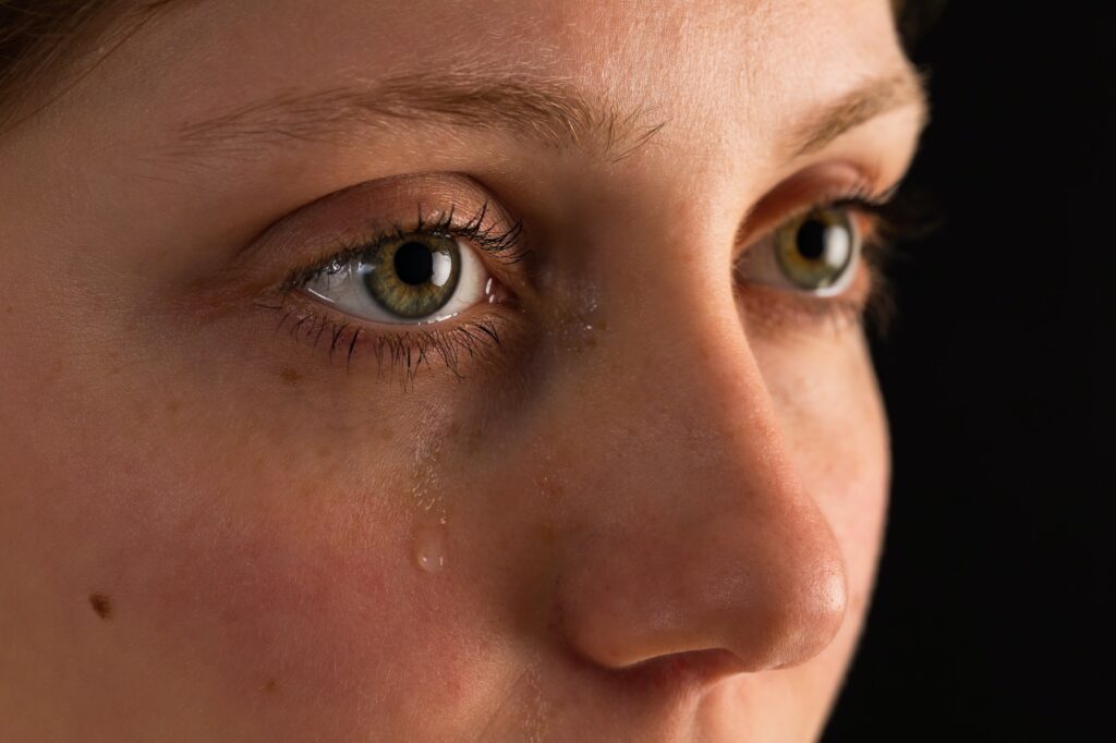 Face of unhappy female in tears from close up in darkness